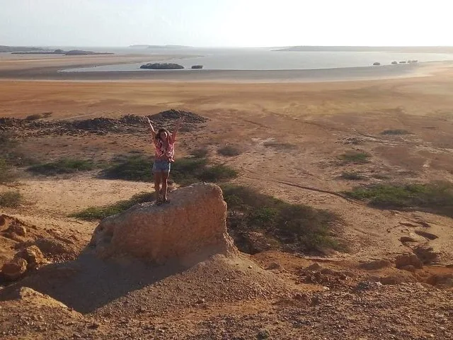 Una donna sta su una roccia con le braccia alzate, ammirando un vasto paesaggio desertico.