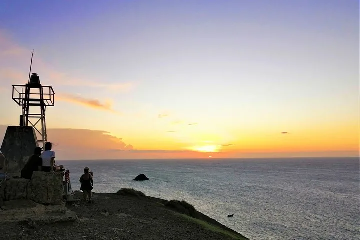 Persone che si godono la vista del tramonto vicino al faro di Cabo de la Vela.