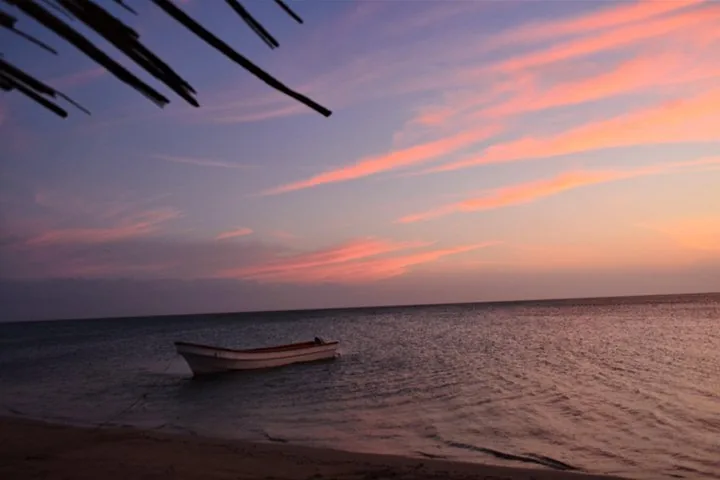 Una piccola barca ancorata nell'acqua calma al crepuscolo, con nuvole rosa.