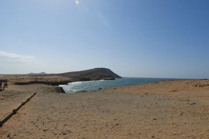 Un paesaggio sabbioso che scende verso una costa rocciosa e l'oceano.