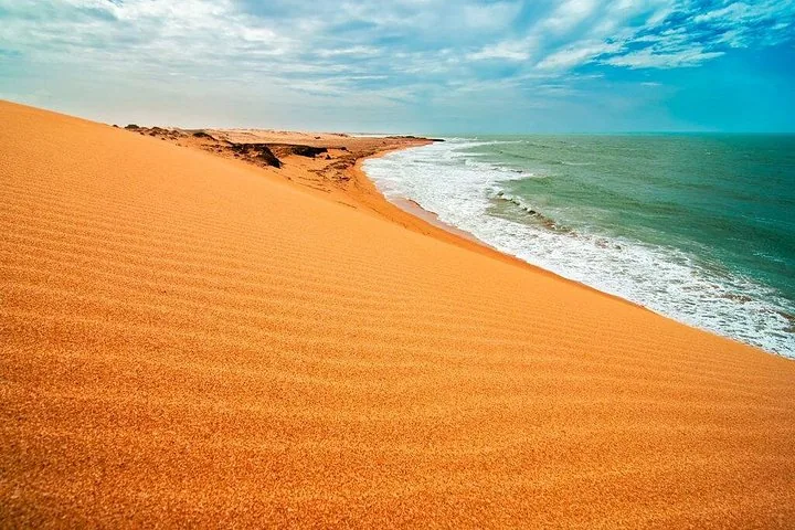 Weite orangefarbene Sanddünen, die sanft abfallen und auf die Wellen des Ozeans treffen.