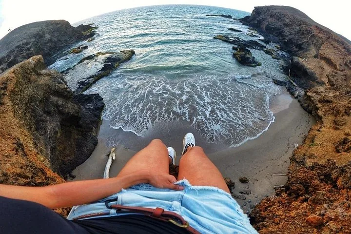 First-person view of someone sitting on a cliff looking down at a rocky cove.