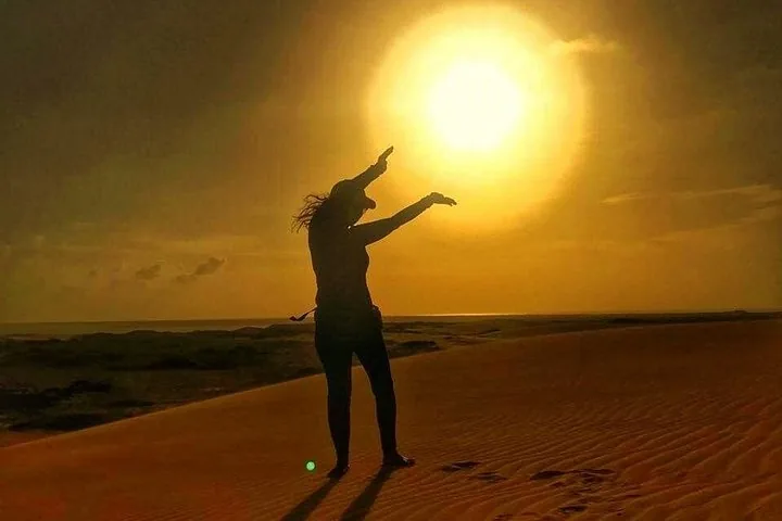 A silhouette of a person posing against a bright sunset in the desert.