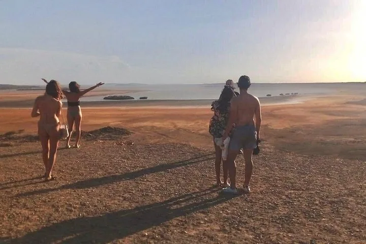 Un gruppo di persone in piedi su una collina rocciosa, con lo sguardo rivolto oltre il deserto verso l'acqua.
